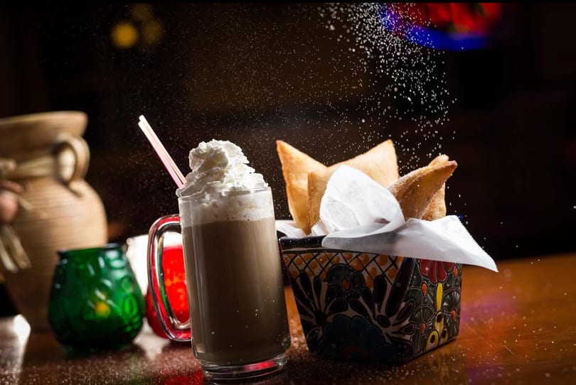 Whipped cream drink and fried pastries in a decorative basket with sugar sprinkling.