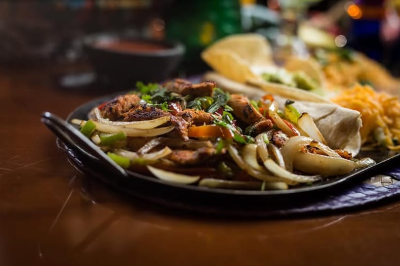 Sizzling plate of chicken fajitas with onions, peppers, tortillas, and shredded cheese.