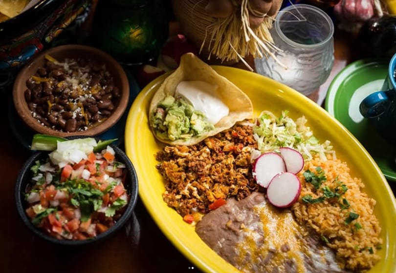 A vibrant Mexican platter with chorizo and eggs, rice, beans, pico de gallo, and a taco.