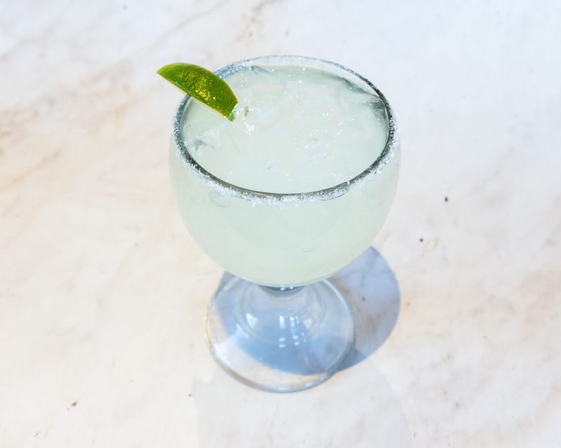 Iced margarita in a glass with a salted rim and lime wedge.